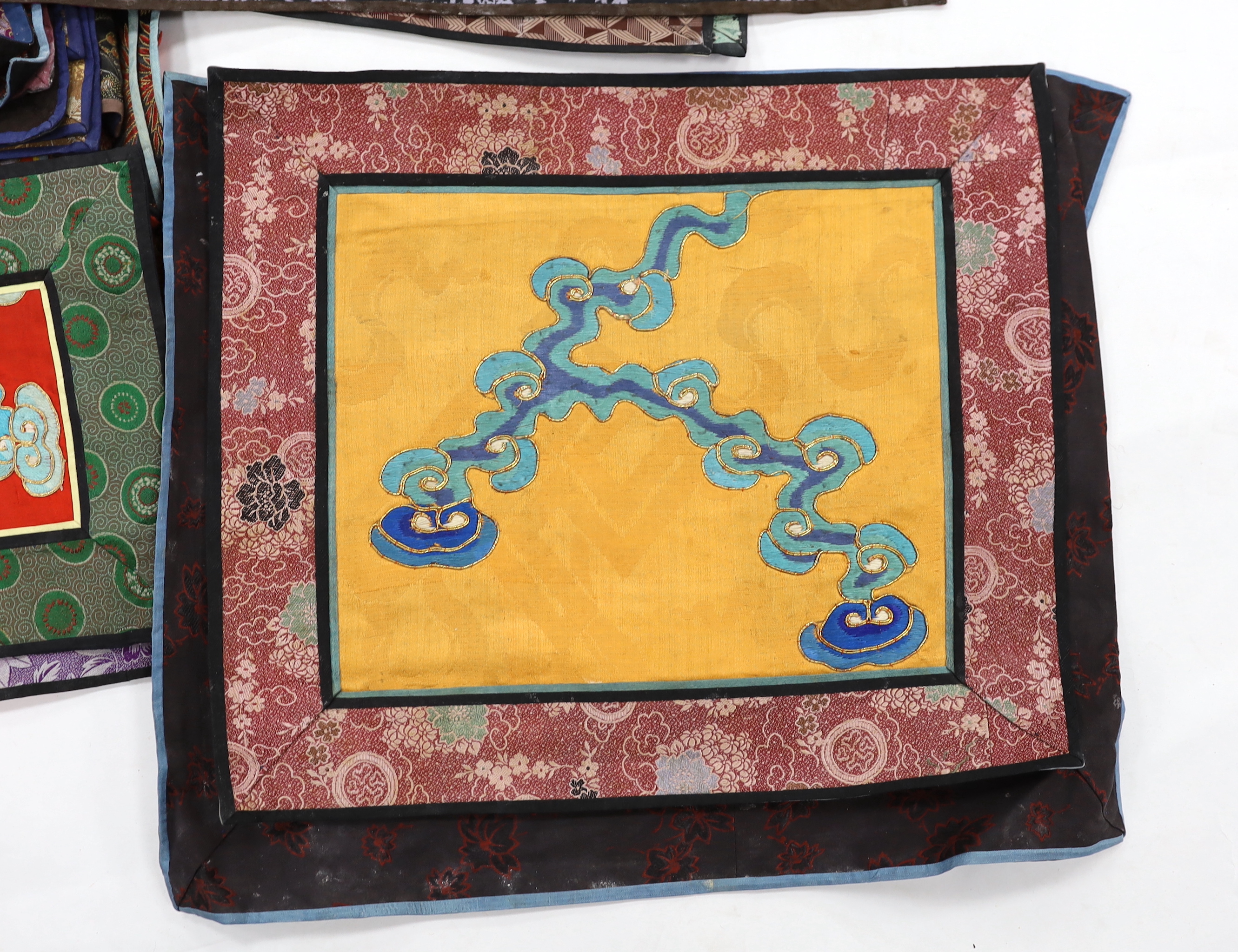 Twenty six assorted Chinese polychrome silk embroidered mats with silk damask borders of varying sizes